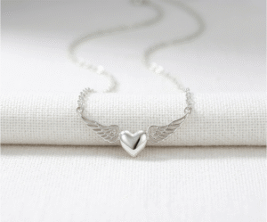 Este collar minimalista plateado simboliza un amor protector que trasciende lo terrenal. Presenta un delicado colgante de corazón pulido flanqueado por alas de ángel detalladas, creando una silueta etérea y atemporal. Fabricado en acero quirúrgico de alta calidad, es una joya resistente y llena de significado, perfecta para llevar como amuleto diario o como un regalo profundamente emocional.