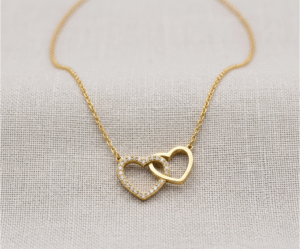 El Collar Corazones Entrelazados es una joya de profundo romanticismo y elegancia contemporánea con un radiante acabado dorado. Destaca por su dije central de dos corazones unidos de forma inseparable: uno con un deslumbrante pavé de cristales y otro de metal liso pulido. Fabricado en acero quirúrgico, es un símbolo perfecto de unión.