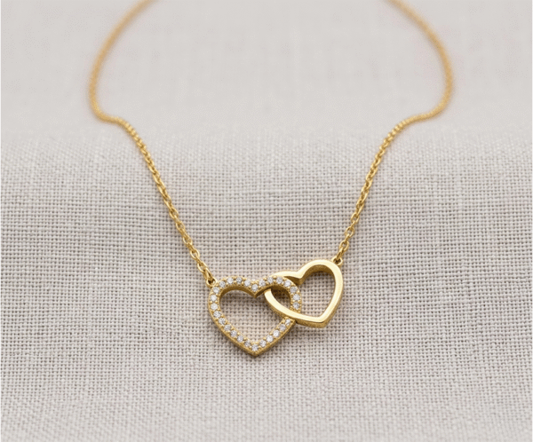 El Collar Corazones Entrelazados es una joya de profundo romanticismo y elegancia contemporánea con un radiante acabado dorado. Destaca por su dije central de dos corazones unidos de forma inseparable: uno con un deslumbrante pavé de cristales y otro de metal liso pulido. Fabricado en acero quirúrgico, es un símbolo perfecto de unión.
