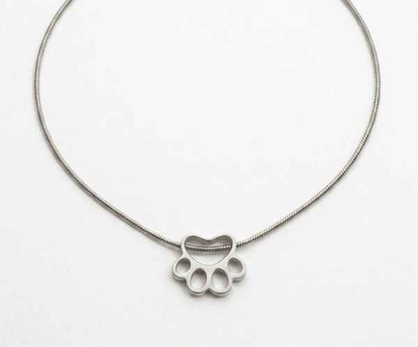 El Collar Huella Minimalista Silver es un tributo elegante al amor incondicional por nuestras mascotas. Presenta un delicado dije calado en forma de huella con acabado pulido espejo, que se desliza sobre una sofisticada cadena tipo serpiente. Fabricado en acero quirúrgico, es una pieza hipoalergénica y resistente, ideal para llevar un recuerdo especial siempre contigo.