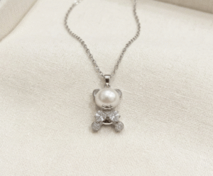 El Collar Osito Perla es una joya tierna y sofisticada que reinterpreta la dulzura con elegancia contemporánea. Destaca por su colgante en forma de osito plateado, cuyo cuerpo es una impecable perla blanca nacarada, complementada con brillantes circonitas facetadas. Fabricado en acero quirúrgico, es un amuleto brillante, resistente y lleno de encanto.