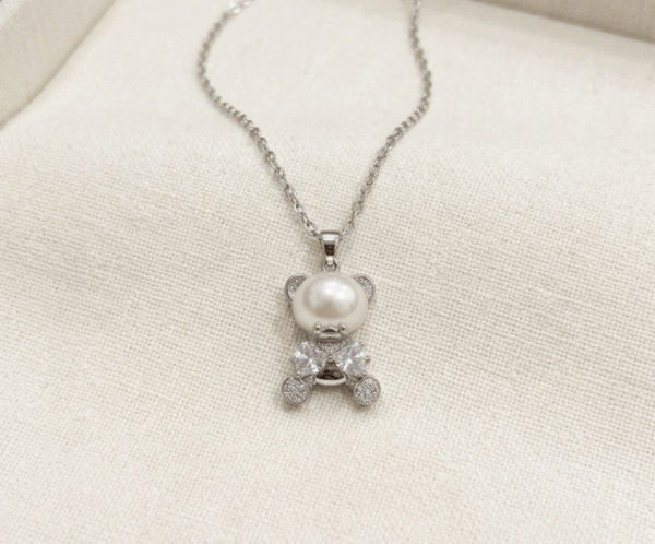 El Collar Osito Perla es una joya tierna y sofisticada que reinterpreta la dulzura con elegancia contemporánea. Destaca por su colgante en forma de osito plateado, cuyo cuerpo es una impecable perla blanca nacarada, complementada con brillantes circonitas facetadas. Fabricado en acero quirúrgico, es un amuleto brillante, resistente y lleno de encanto.