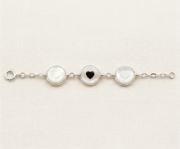 La Pulsera Aros con Corazón es una pieza de exquisita dulzura y acabado artesanal con un brillo plateado impecable. Destaca por tres medallones circulares de nácar natural que albergan delicados corazones en su centro, unidos por una elegante cadena de eslabones. Fabricada en acero quirúrgico, combina romanticismo y luz con un estilo atemporal.