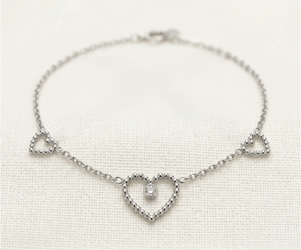 La Pulsera Corazón Central es una joya de elegancia sublime con un acabado plateado brillante. Presenta un corazón central calado con un cristal solitario engastado, escoltado por dos corazones laterales de diseño perlado sobre una delicada cadena de eslabones. Fabricada en acero quirúrgico, es el accesorio perfecto para un estilo romántico y sofisticado.