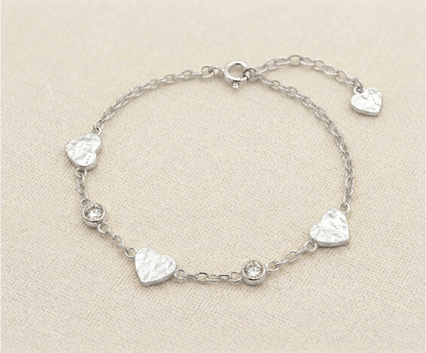 La Pulsera Corazón Colgante es una pieza de encanto artesanal y brillo sutil con un acabado plateado impecable. Presenta delicados dijes de corazón con una textura martillada única, intercalados con cristales brillantes sobre una cadena de eslabones. Fabricada en acero quirúrgico, combina romanticismo y modernidad, ofreciendo un estilo sofisticado para cualquier ocasión.