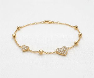 La Pulsera Corazón de Cristales es una pieza deslumbrante que combina romanticismo y lujo. Presenta dos dijes de corazón con un exquisito pavé de cristales brillantes, intercalados con esferas pulidas sobre una delicada cadena dorada. Fabricada en acero quirúrgico, es la joya perfecta para quienes buscan un brillo sofisticado y duradero.