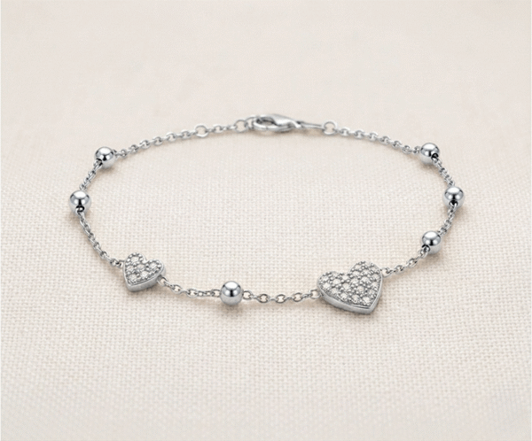 La Pulsera Corazón de Cristales es una pieza deslumbrante que combina romanticismo y lujo en un acabado plateado impecable. Presenta dos dijes de corazón con un exquisito pavé de cristales brillantes, intercalados con esferas pulidas sobre una delicada cadena. Fabricada en acero quirúrgico, es la joya perfecta para un brillo sofisticado y duradero.