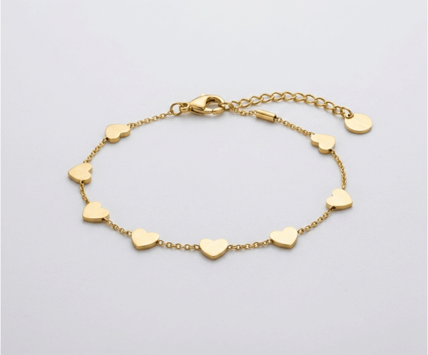 La Pulsera Corazones En Cadena es una joya de encanto romántico y sofisticación minimalista con un radiante acabado dorado. Destaca por su hilera perimetral de ocho corazones lisos y pulidos, integrados de forma fija sobre una sutil cadena de eslabones. Fabricada en acero quirúrgico, es el accesorio perfecto para el día a día.