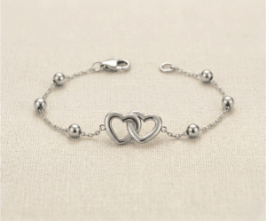 La Pulsera Corazones Entrelazados es una joya llena de significado y elegancia atemporal con un acabado plateado impecable. Presenta un dije central de dos corazones calados íntimamente unidos, acompañados por delicadas esferas pulidas sobre una fina cadena. Fabricada en acero quirúrgico, es el accesorio perfecto para simbolizar la unión eterna con sofisticación.