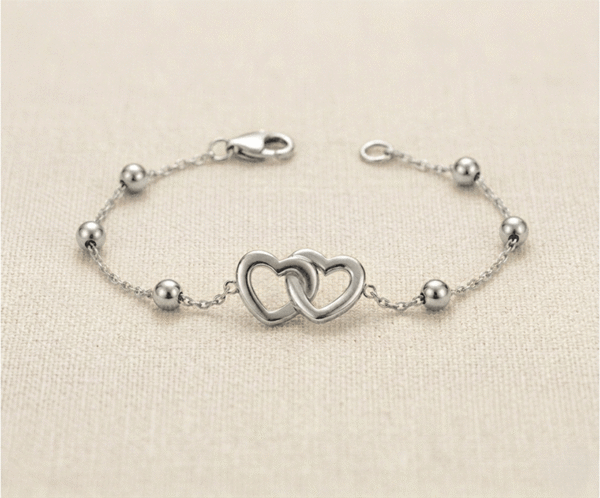 La Pulsera Corazones Entrelazados es una joya llena de significado y elegancia atemporal con un acabado plateado impecable. Presenta un dije central de dos corazones calados íntimamente unidos, acompañados por delicadas esferas pulidas sobre una fina cadena. Fabricada en acero quirúrgico, es el accesorio perfecto para simbolizar la unión eterna con sofisticación.