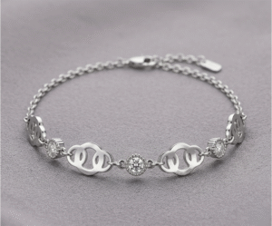 La Pulsera Corona de Brillos es una joya de elegancia majestuosa con un impecable acabado plateado. Presenta una secuencia de eslabones calados con formas curvas, intercalados con cristales solitarios engastados en biseles perlados que capturan la luz intensamente. Fabricada en acero quirúrgico, es la pieza ideal para un estilo sofisticado y atemporal.