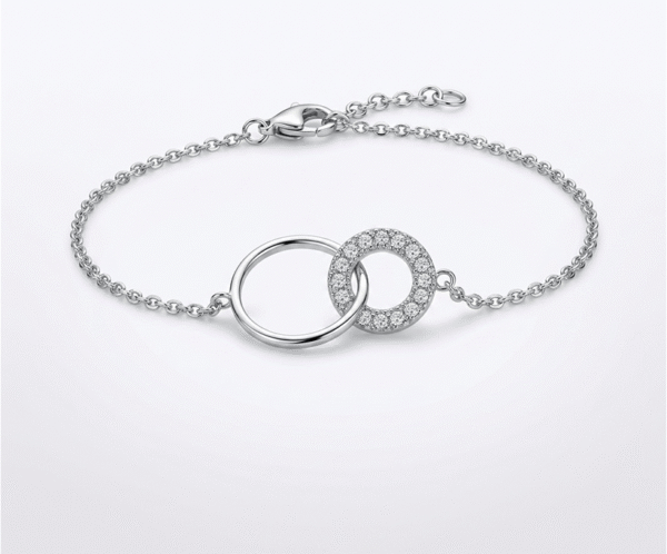 La Pulsera Dúo de Aros es un símbolo de unión eterna y sofisticación moderna. Presenta dos anillos entrelazados: uno de acabado pulido liso y otro adornado con un pavé de cristales brillantes que capturan la luz. Fabricada en acero quirúrgico plateado, es la pieza ideal para quienes buscan un accesorio significativo con un brillo lujoso y duradero.