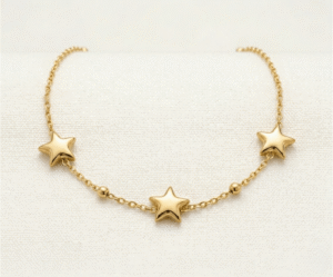 La Pulsera Estrella Fugaz es una pieza mágica que captura la esencia del cosmos. Presenta tres estrellas de cinco puntas con relieve suave, intercaladas con delicadas esferas pulidas en una cadena de eslabones finos. Fabricada en acero quirúrgico con un lujoso baño dorado, es una joya radiante y resistente que simboliza sueños y deseos.