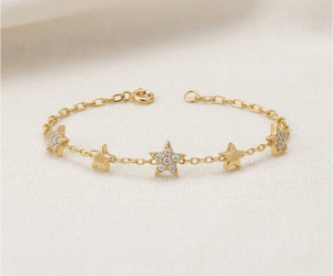 La Pulsera Estrellas de Cristales es una pieza radiante con un sofisticado acabado dorado que captura la esencia del cosmos. Presenta tres estrellas centrales con un brillante pavé de cristales, escoltadas por dos estrellas lisas sobre una delicada cadena de eslabones. Fabricada en acero quirúrgico, combina elegancia y luz con distinción.
