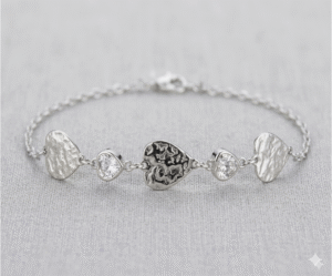 La Pulsera Gotas de Cristal es una pieza de diseño artístico y acabado plateado envejecido que destaca por su carácter único. Combina tres dijes de corazón con una textura orgánica martillada e irregular, intercalados con dos cristales brillantes facetados de gran pureza. Fabricada en acero quirúrgico, ofrece un estilo bohemio y sofisticado.