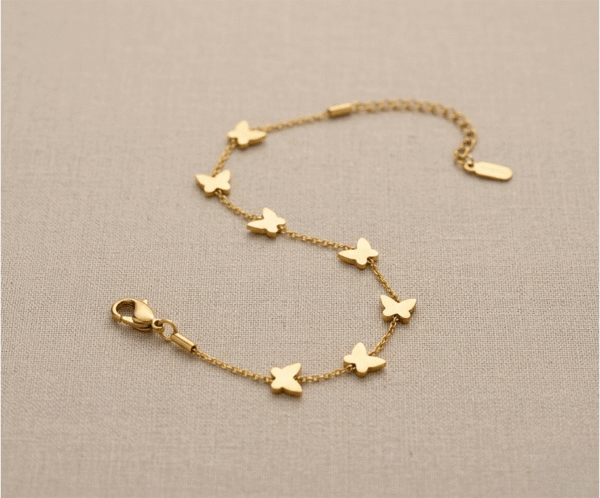 Pulsera Mariposas en Cadena _E101 La Pulsera Mariposas en Cadena es una joya de encanto natural y sofisticación minimalista con un radiante acabado dorado. Destaca por su hilera perimetral de ocho mariposas lisas y pulidas, integradas de forma fija sobre una sutil cadena de eslabones. Fabricada en acero quirúrgico, es el accesorio perfecto para el día a día.
