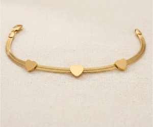 La Pulsera Rígida con Corazones es una pieza de elegancia minimalista y diseño contemporáneo con un sofisticado acabado dorado. Destaca por sus tres corazones lisos integrados en una moderna cadena plana de estilo "snake" que se adapta con suavidad a la muñeca. Fabricada en acero quirúrgico, ofrece un brillo lujoso y duradero.