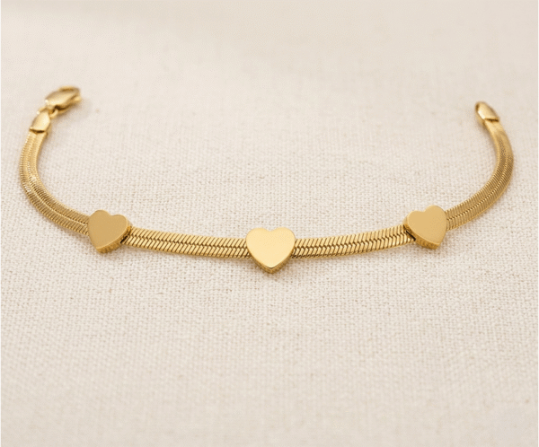 La Pulsera Rígida con Corazones es una pieza de elegancia minimalista y diseño contemporáneo con un sofisticado acabado dorado. Destaca por sus tres corazones lisos integrados en una moderna cadena plana de estilo "snake" que se adapta con suavidad a la muñeca. Fabricada en acero quirúrgico, ofrece un brillo lujoso y duradero.