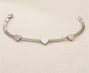 La Pulsera Rígida con Corazones es una pieza de elegancia minimalista y diseño contemporáneo, disponible en acabados dorado y plateado. Destaca por sus tres corazones lisos integrados en una sofisticada cadena plana de estilo "snake" que se adapta con suavidad. Fabricada en acero quirúrgico, ofrece un brillo espejo duradero y versatilidad absoluta.
