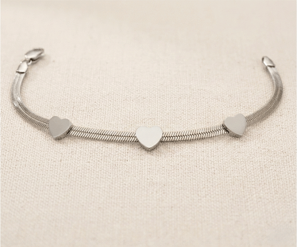La Pulsera Rígida con Corazones es una pieza de elegancia minimalista y diseño contemporáneo, disponible en acabados dorado y plateado. Destaca por sus tres corazones lisos integrados en una sofisticada cadena plana de estilo "snake" que se adapta con suavidad. Fabricada en acero quirúrgico, ofrece un brillo espejo duradero y versatilidad absoluta.