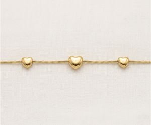 La Pulsera Trio de Corazones es una pieza de elegancia minimalista y acabado impecable. Presenta tres corazones con volumen y relieve suave, integrados armoniosamente en una sofisticada cadena de estilo serpiente. Fabricada en acero quirúrgico con un lujoso baño dorado, es una joya moderna y versátil, ideal para simbolizar vínculos especiales con una discreción sofisticada.