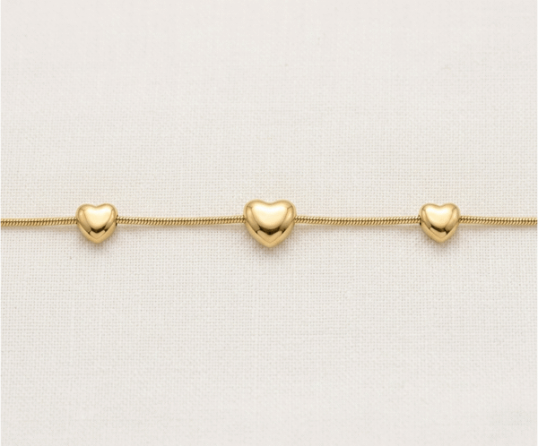 La Pulsera Trio de Corazones es una pieza de elegancia minimalista y acabado impecable. Presenta tres corazones con volumen y relieve suave, integrados armoniosamente en una sofisticada cadena de estilo serpiente. Fabricada en acero quirúrgico con un lujoso baño dorado, es una joya moderna y versátil, ideal para simbolizar vínculos especiales con una discreción sofisticada.