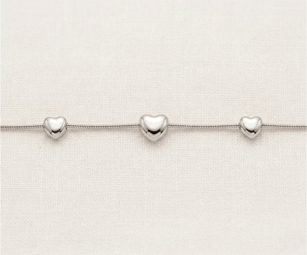 La Pulsera Trio de Corazones es una pieza de elegancia minimalista con un impecable acabado plateado. Presenta tres corazones con volumen y relieve suave, integrados armoniosamente en una sofisticada cadena de estilo serpiente. Fabricada en acero quirúrgico, es una joya moderna y versátil, ideal para simbolizar vínculos especiales con una discreción sofisticada y duradera.